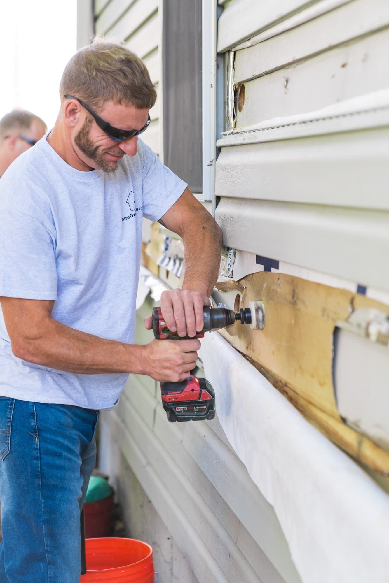 Technician drilling access holes in wood siding